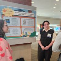 Jaimee Achley talking to two students in front of their poster presentation.